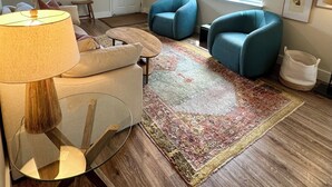 Un soggiorno con un divano, due poltrone, un tavolino, una lampada, un tappeto e una porta.