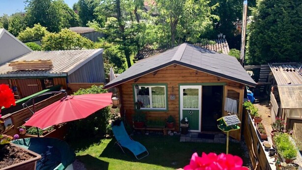 Ein kleines Holzhaus mit einer Rutsche, einem roten Regenschirm und einem Garten mit Topfpflanzen.