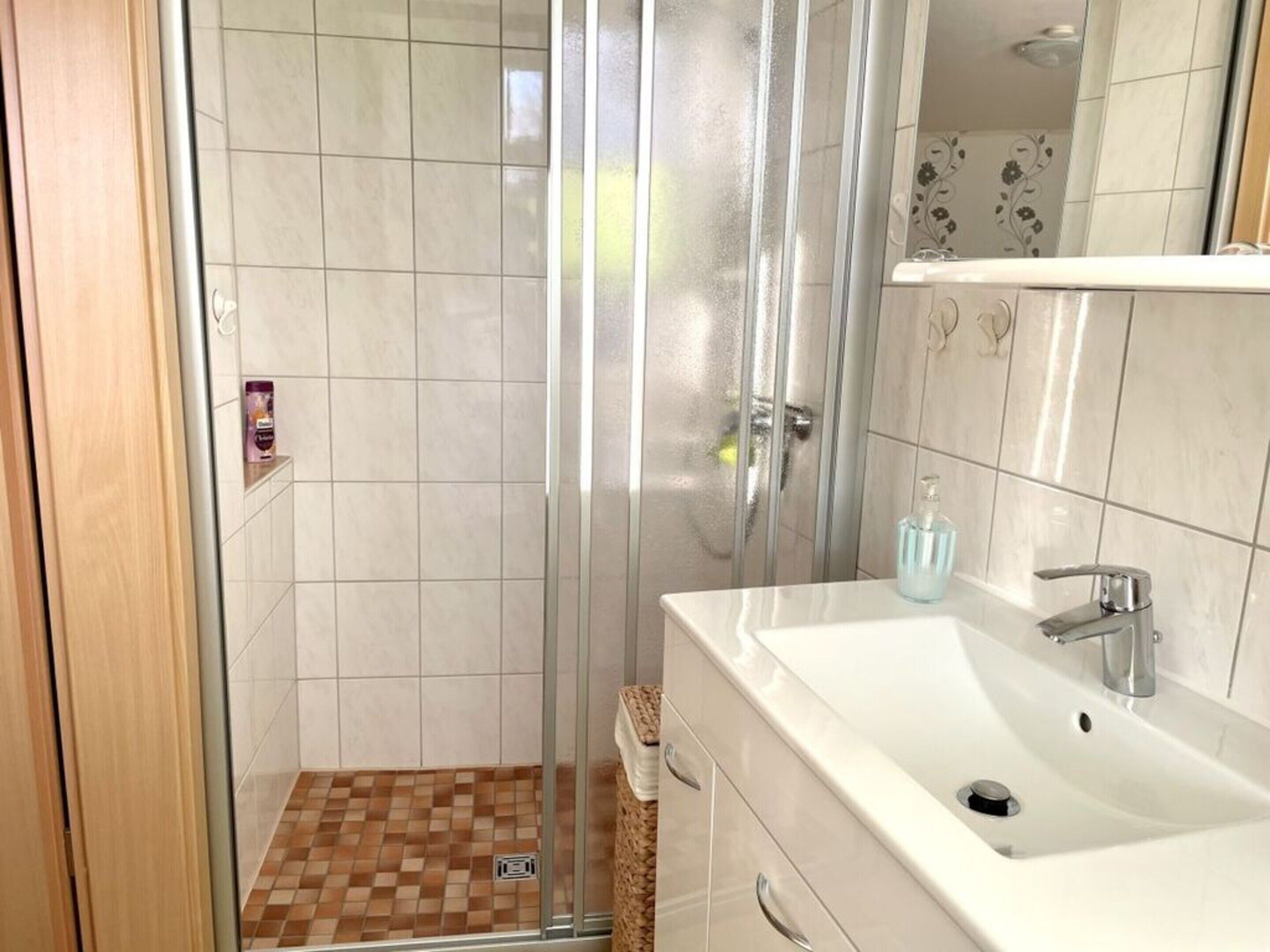 Un baño con cabina de ducha de vidrio, un lavabo blanco y un espejo encima.