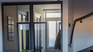 Un intérieur moderne avec un escalier, une plante en pot et une vue sur une pièce où se trouve un porte-manteau.