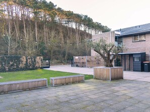 A courtyard with a paved area, wooden benches, a brick building, and a tree.