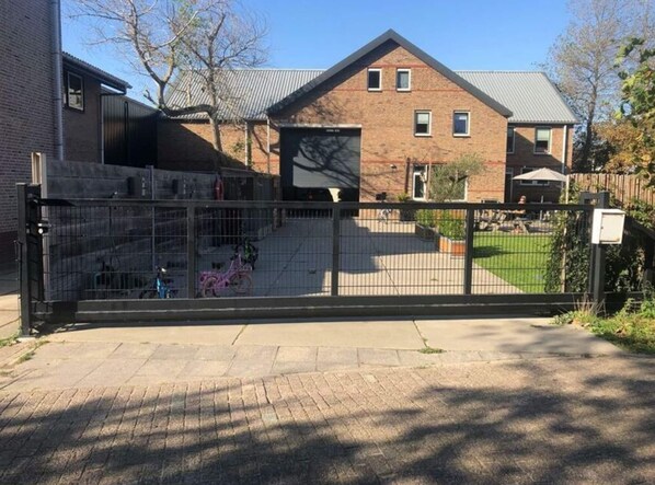 A gated residential area with a brick house, a fenced yard, and a bicycle.