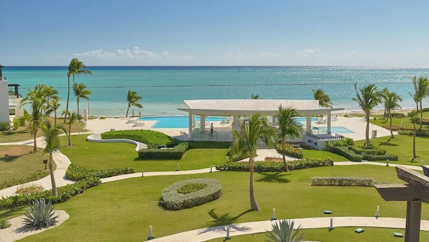 Um resort com piscina, palmeiras e vista para o oceano.