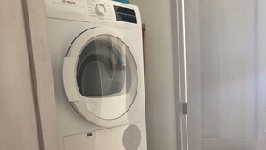 Máquina de lavar e secar empilhadas numa lavanderia, com uma porta ao fundo.