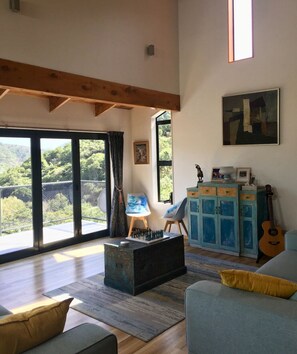 Relax in this stylish living room with a high ceiling, sofa, armchairs, and a balcony overlooking lush greenery.