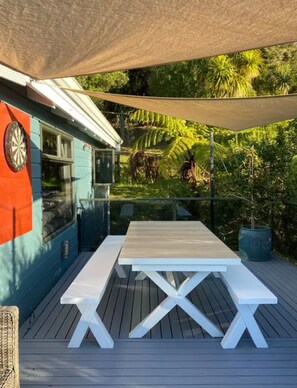 Relax in the serene outdoor patio area, complete with a picnic table and benches, surrounded by lush greenery and a shaded canopy.
