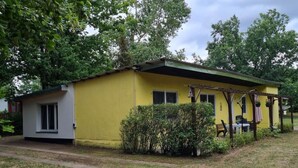 Ein gelbes Einfamilienhaus mit einer kleinen Veranda und einer überdachten Sitzgruppe im Freien.