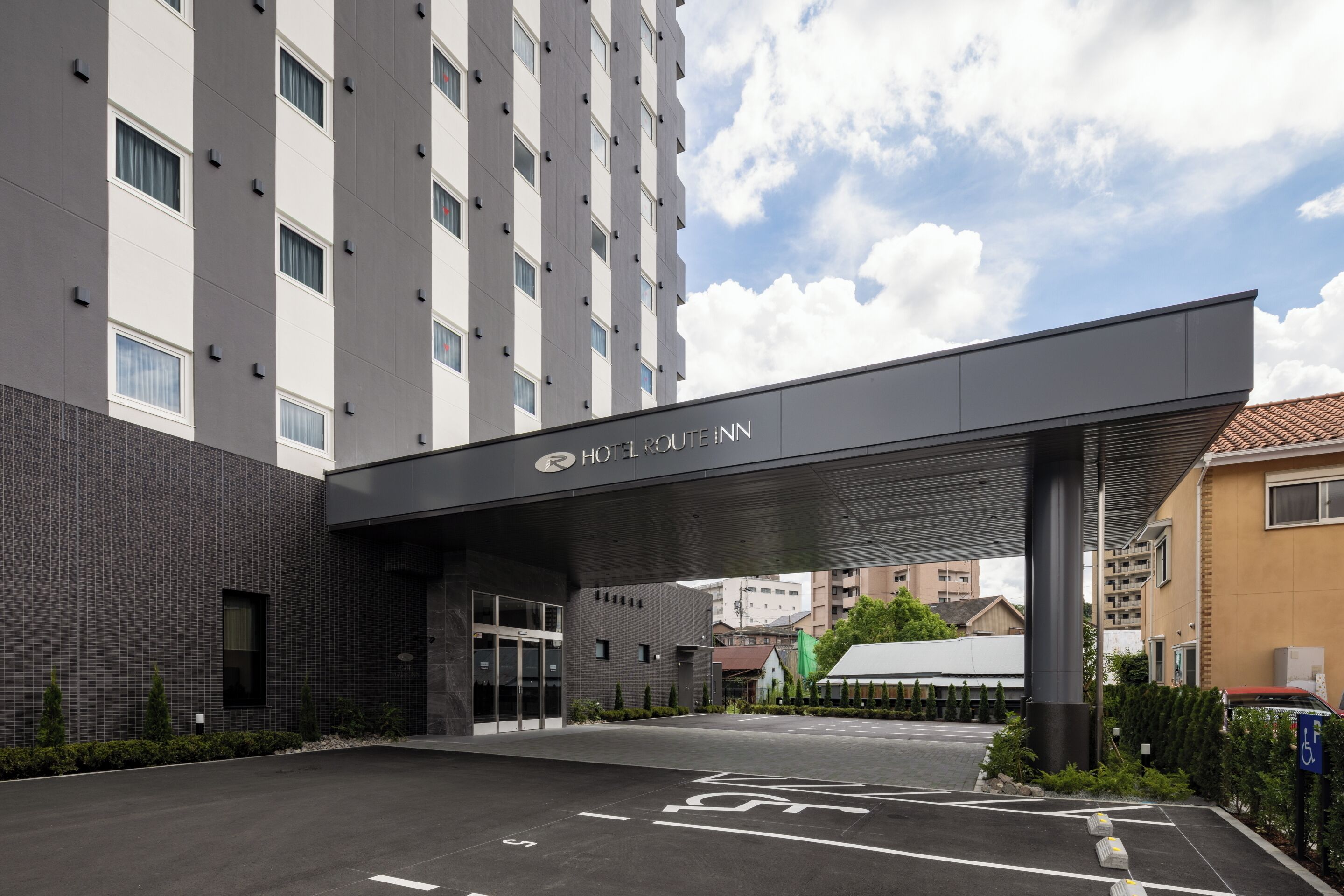 A modern hotel entrance with a covered walkway, a parking area, and a clear view of the surrounding buildings.