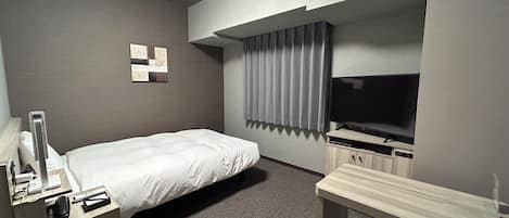 A hotel room with a bed, a desk, a television, and a wall-mounted light fixture.