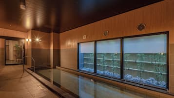 A modern indoor pool area with a wooden ceiling, large windows with frosted glass, and a clear view of bamboo outside.