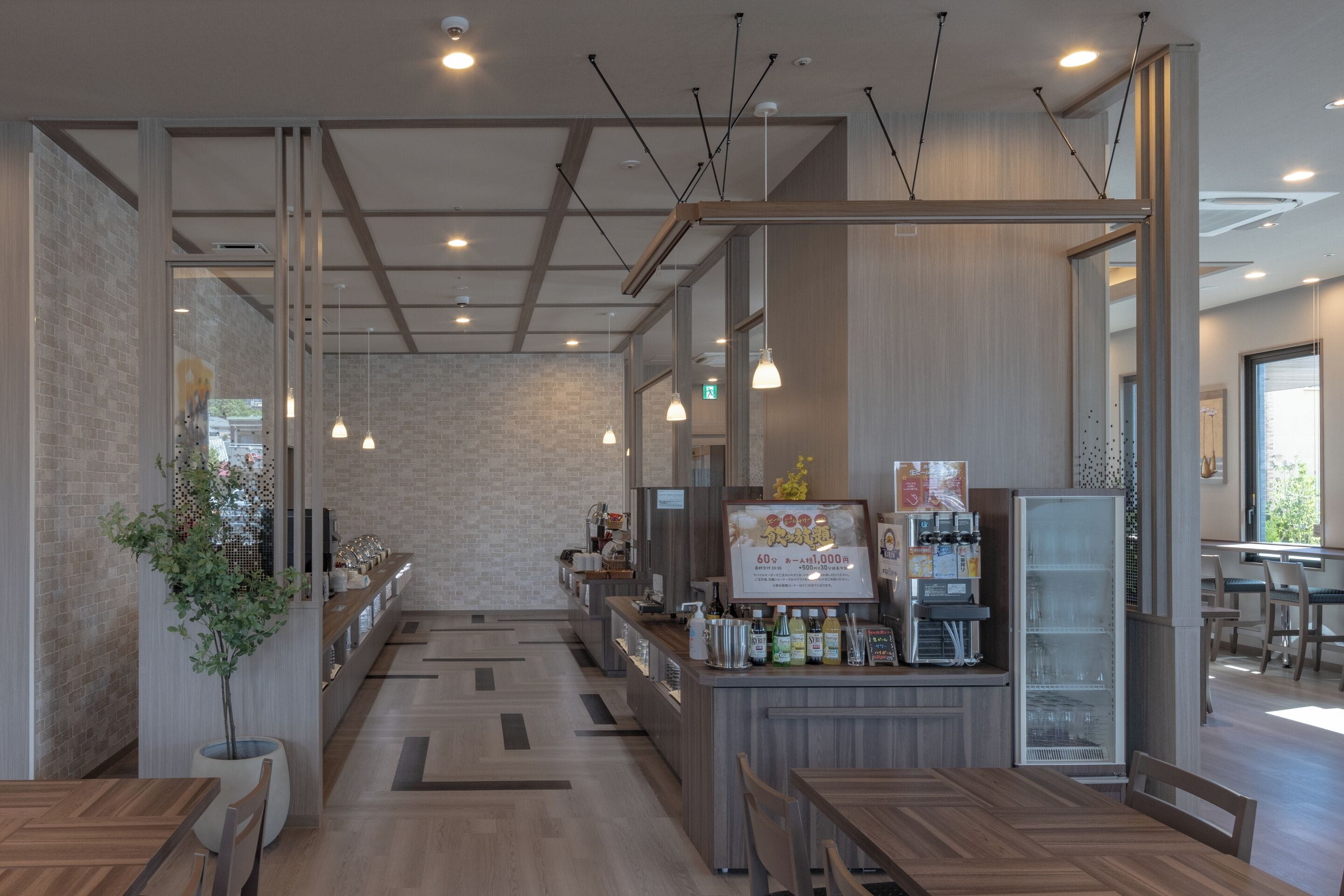 A modern cafe with wooden furniture, a bar area, and a refrigerator stocked with beverages.