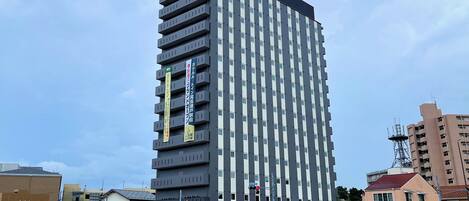 Un grand immeuble d’hôtel, avec de nombreux étages et des balcons, un ciel dégagé et un parking rempli de voitures.