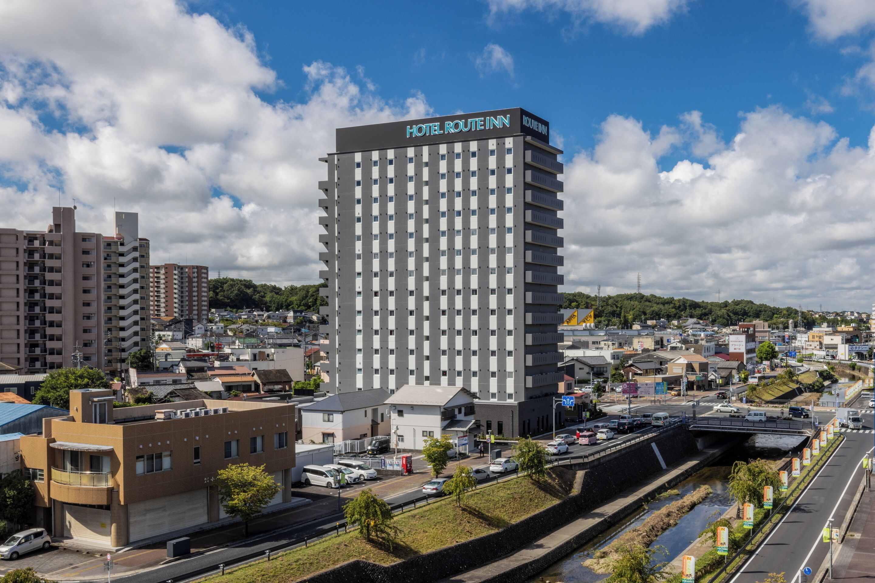 A modern hotel with a prominent sign, surrounded by urban buildings and a clear sky.