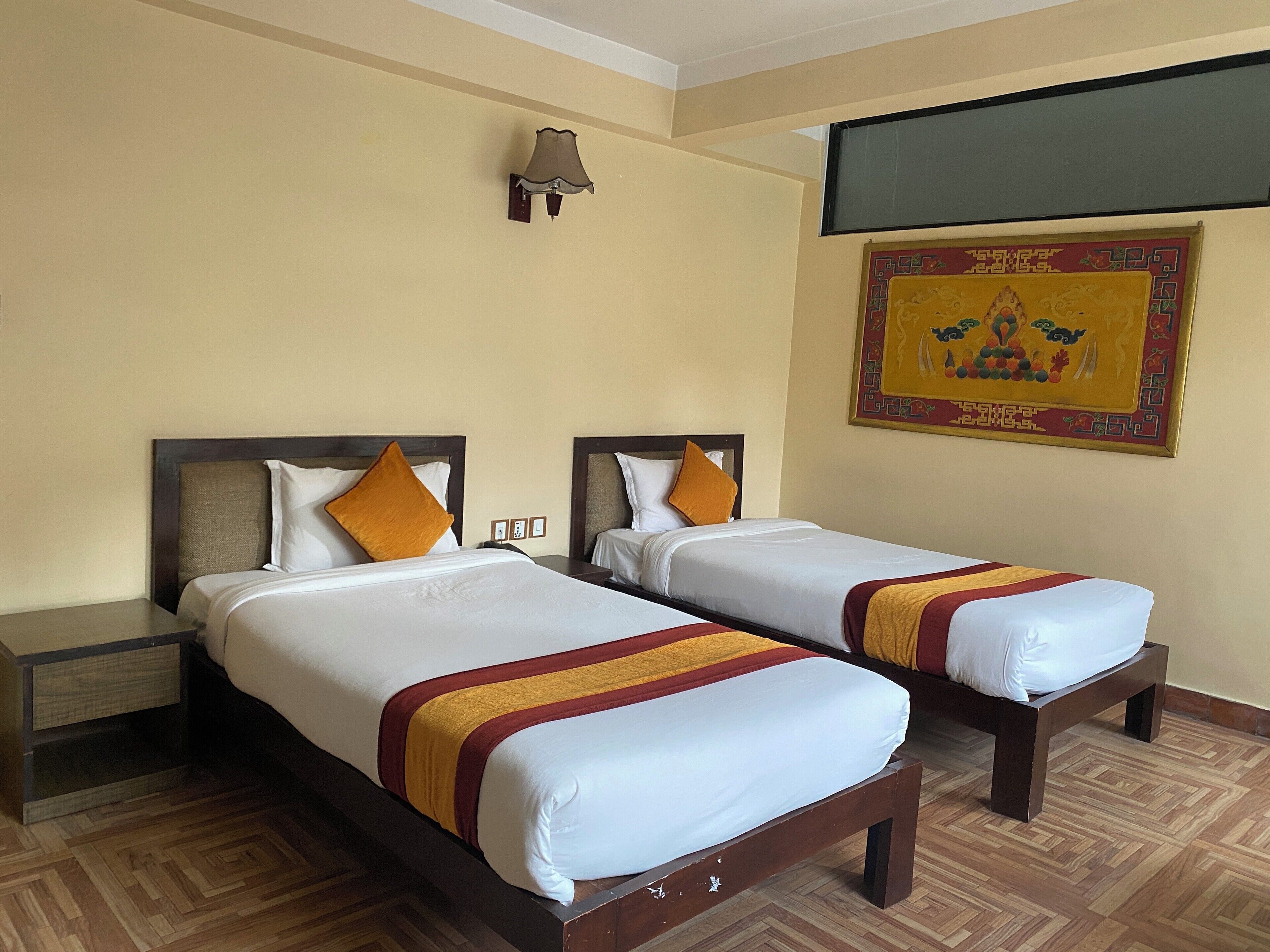 Habitación de hotel con dos camas, cabeceros de madera, ropa de cama blanca y un adorno colgante en la pared.