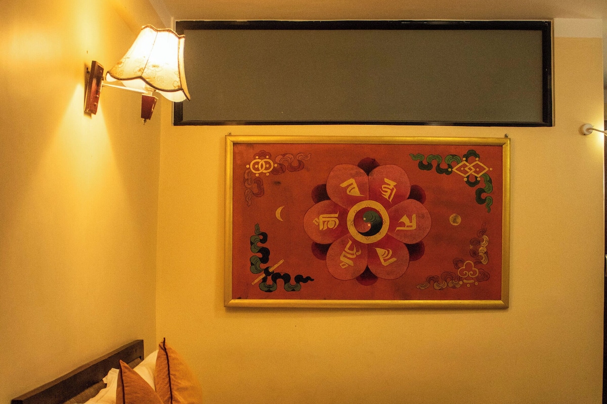 A hotel room with a bed, pillows, a bedside table with a lamp, and a wall decoration.