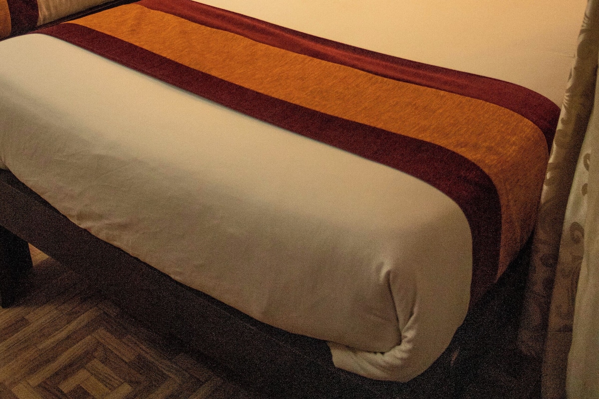 Two single beds with wooden headboards, white bedding, and orange throw pillows.