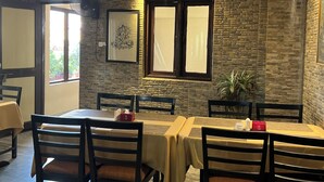 A dining area with a stone wall, wooden chairs, and tables. - Boudha Stupa View Guest House (Kathmandu)
