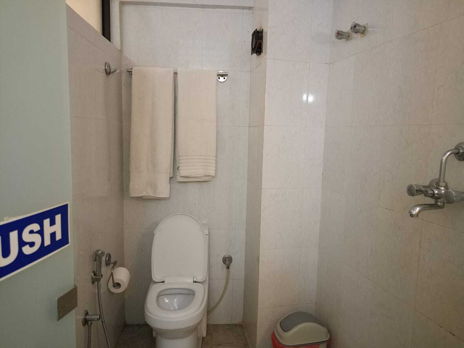Ein kleines, kompaktes Badezimmer mit Toilette, Dusche und Waschbecken. Über der Toilette befindet sich ein Handtuchhalter und neben dem Waschbecken ein Mülleimer.