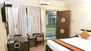 A hotel room with a bed, a desk, a chair, a fan, and a view of the outside. - Boudha Stupa View Guest House (Kathmandu)