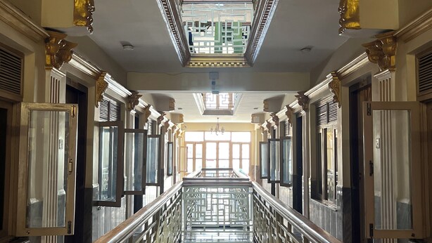 A grand hallway with ornate columns, a glass railing, and a skylight. - Boudha Stupa View Guest House (Kathmandu)