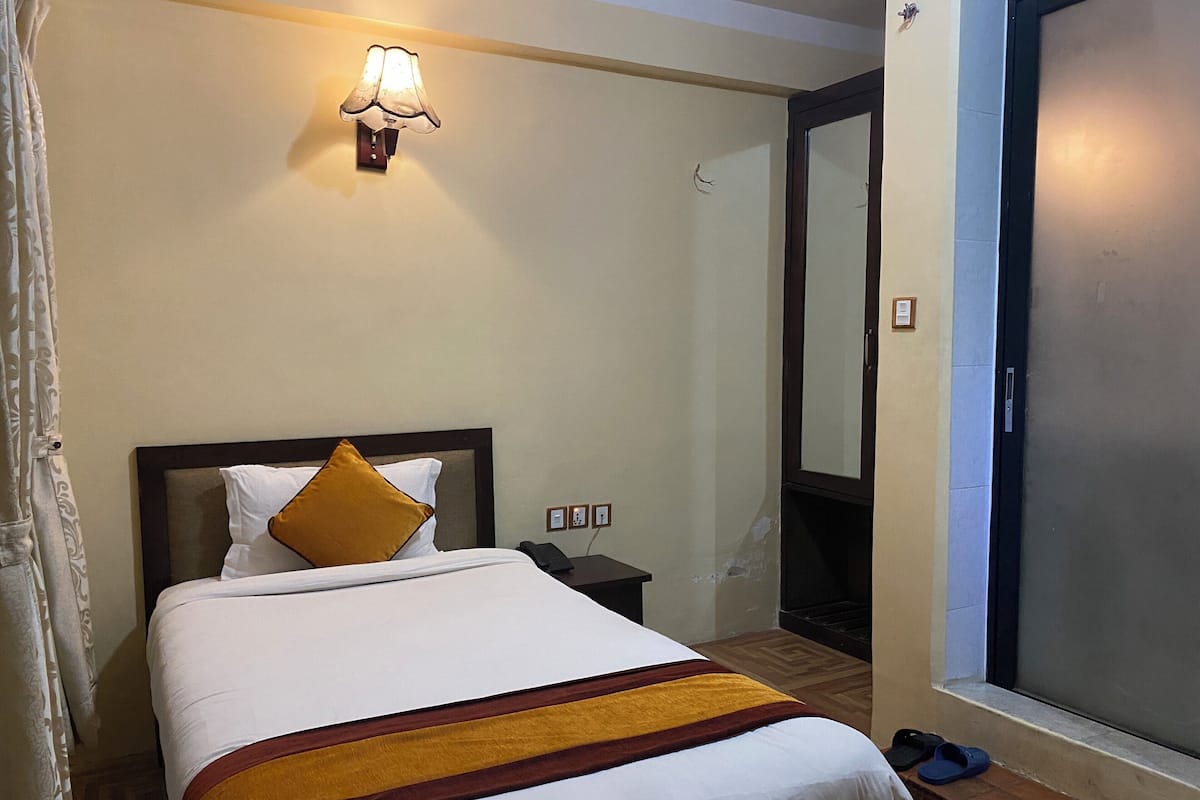 A hotel room with a bed, a nightstand, a lamp, a mirror, and a window with a view.
