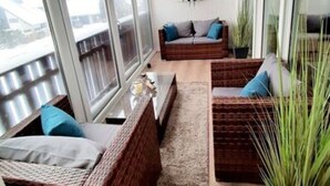 Ein Balkon mit Korbmöbeln, einer Wanduhr und Topfpflanzen.