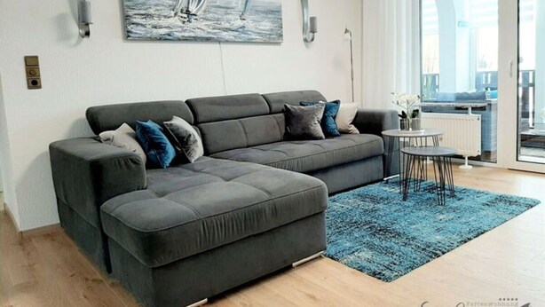Ein modernes Wohnzimmer mit einem grauen Ecksofa, einem blauen Teppich und einem Gemälde eines Segelboots an der Wand.