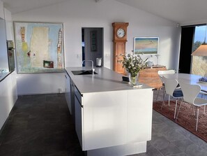 Une cuisine moderne avec un îlot central, un coin repas comprenant une table et des chaises, une horloge et un tableau accroché au mur.