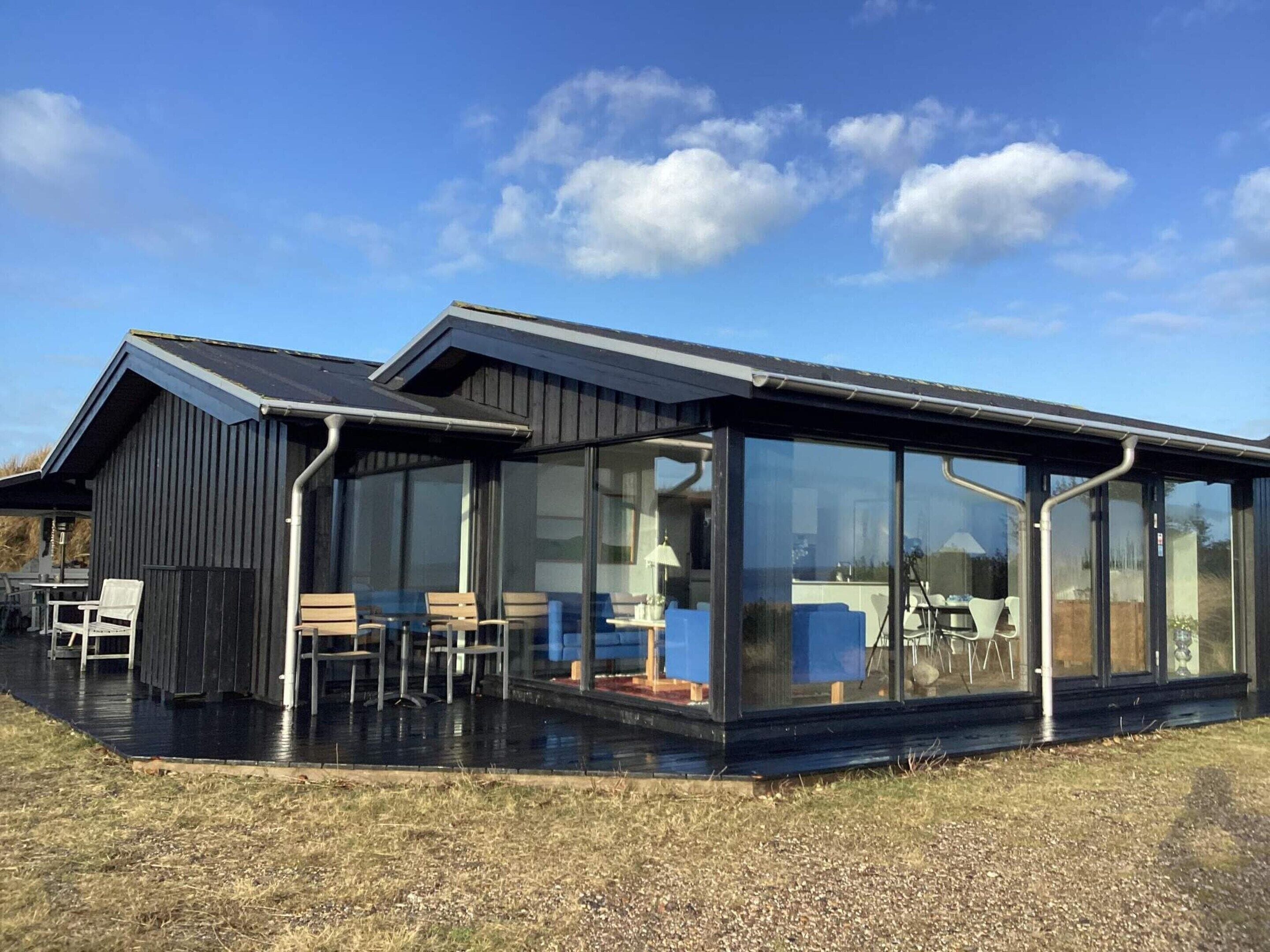 Un bâtiment moderne doté d’une extension en verre, d’une terrasse et d’un toit en métal.