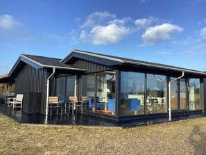 Un bâtiment moderne doté d’une extension en verre, d’une terrasse et d’un toit en métal.