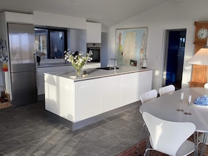 A modern kitchen with a central island, stainless steel appliances, and a dining area with white chairs. - 4 Star Holiday Home in Hvide Sande (Hvide Sande)