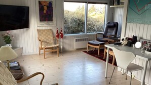 A room with a wooden floor, a television mounted on the wall, a desk with a chair, and a window with a view of trees. - 4 Star Holiday Home in Hvide Sande (Hvide Sande)