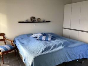 Une chambre à coucher comprenant un lit, une chaise, une étagère avec des objets décoratifs et une armoire.