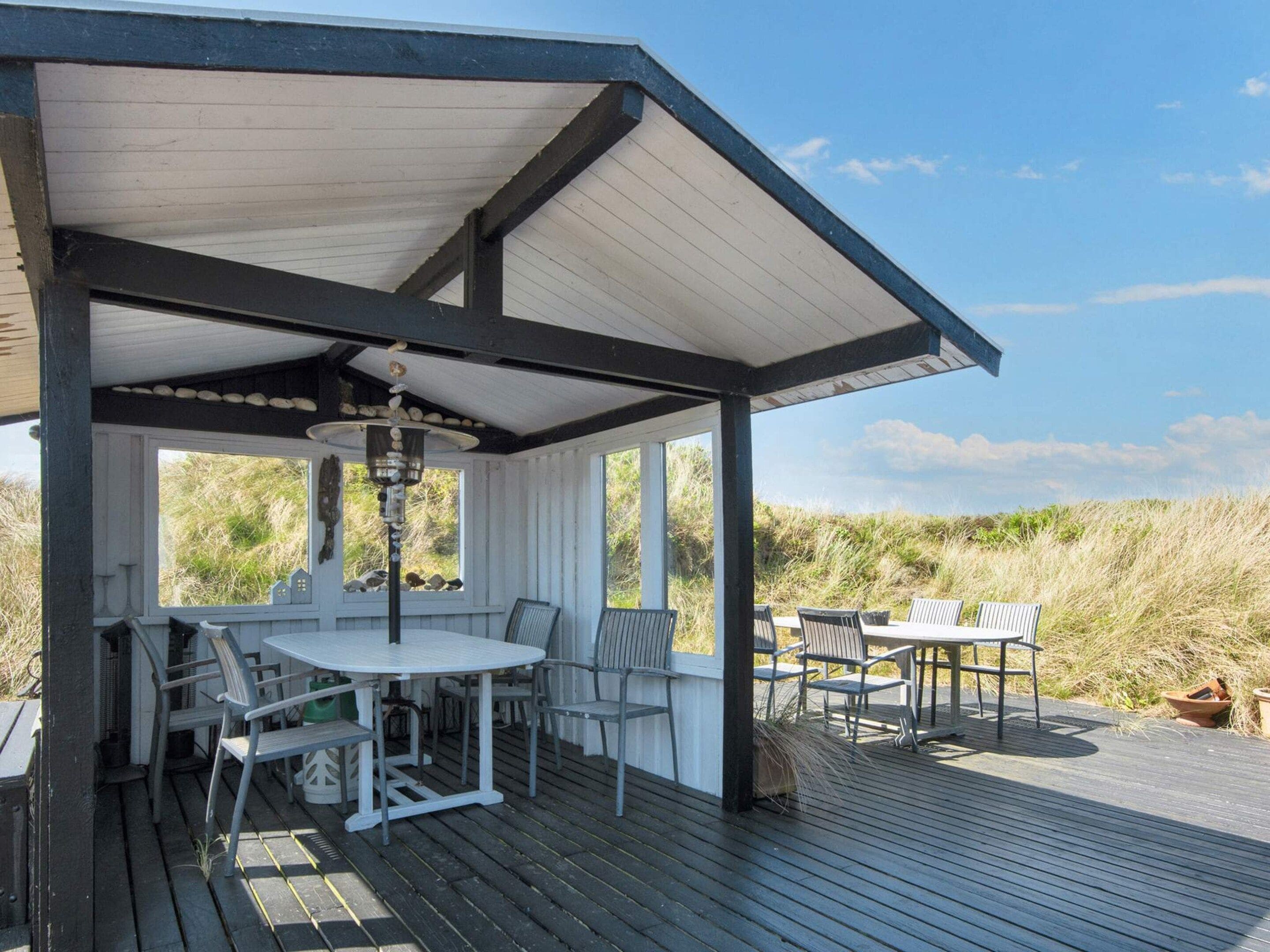 A covered outdoor seating area with a table and chairs, overlooking a natural landscape.