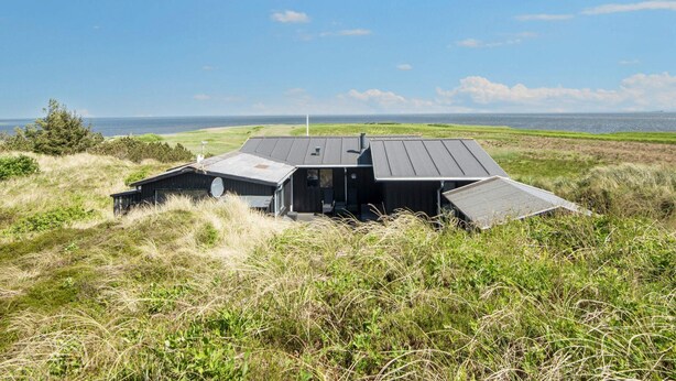 A modern house with a sloped roof, situated in a grassy field with a view of the ocean. - 4 Star Holiday Home in Hvide Sande (Hvide Sande)