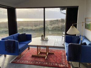 A modern living room with a large window, two blue sofas, a wooden coffee table, and a red patterned rug. - 4 Star Holiday Home in Hvide Sande (Hvide Sande)