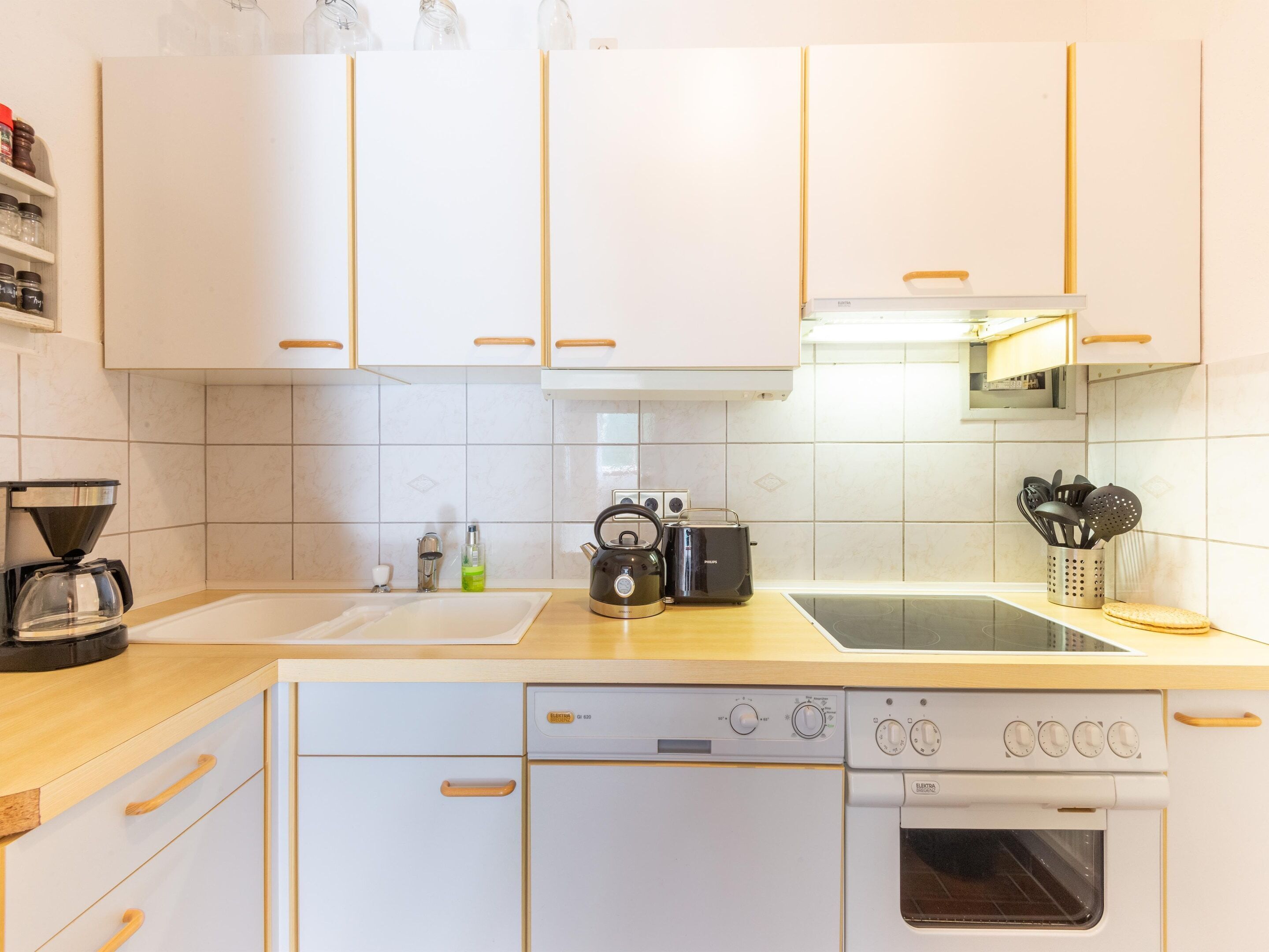 Eine moderne Küche mit weißen Schränken, einer Kaffeemaschine, einem Wasserkocher, einem Toaster und einem Geschirrspüler.