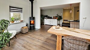 Un salon moderne avec un poêle à bois, une table à manger et un coin cuisine visible à travers une porte ouverte.