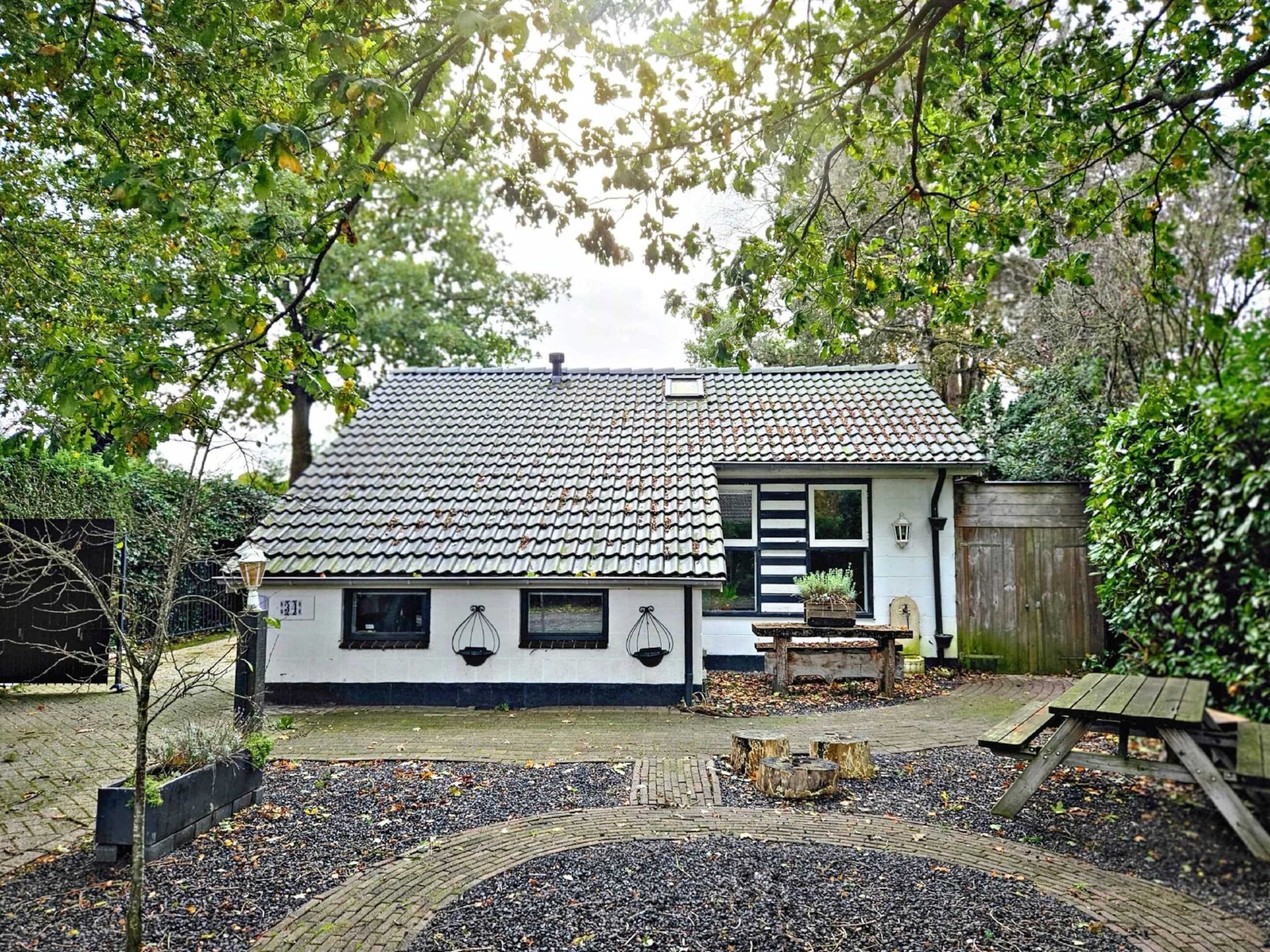 Una casa tradicional japonesa con tejado de tejas, cerca de madera y un jardín con caminos de grava y un banco de madera.