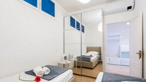 A hotel room with two beds, a large mirror, a small table with a fan, and a view into the adjacent room. - Cozy Maria Apartment in Portofino, Portofino, Italy (Portofino)