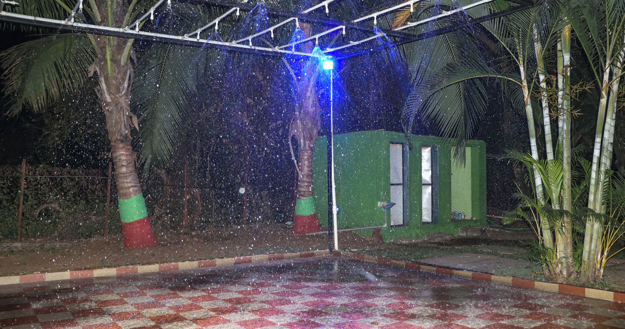 A water feature with a blue light, surrounded by palm trees and a green structure.
