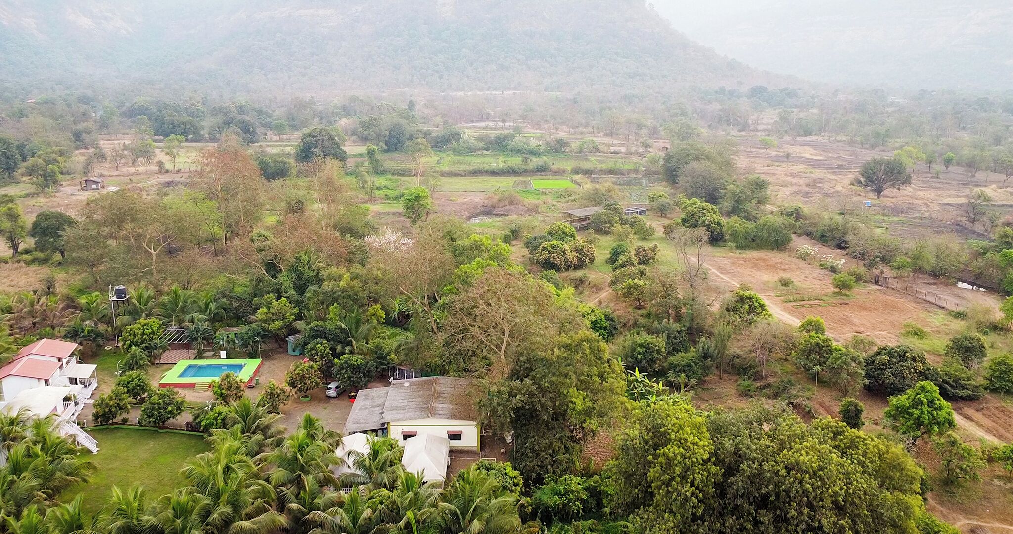 Paisaje rural con casas dispersas, una piscina y abundante vegetación.