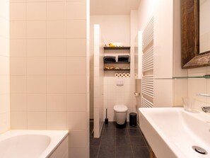 A modern bathroom with a bathtub, toilet, and shelves with toiletries.