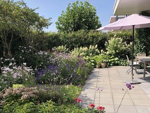 A garden with a variety of flowers and plants, a paved patio, and outdoor furniture.