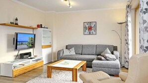 A modern living room with a grey sofa, a wooden coffee table, a flat-screen TV, and a decorative clock on the wall. - Holiday Apartment Sanddorn WE 7 (Boergerende-Rethwisch)