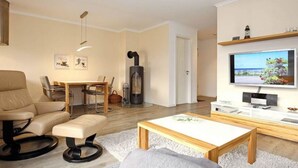 A modern living room with a sofa, a dining table, a TV, and a fireplace. - Holiday Apartment Sanddorn WE 7 (Boergerende-Rethwisch)