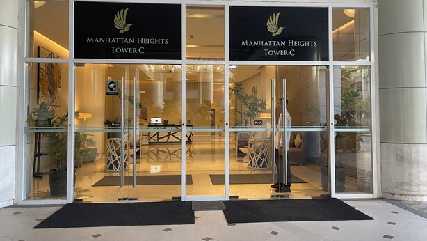 The entrance to Manhattan Heights Tower C with a glass facade, a reception desk, and a push button for entry.
