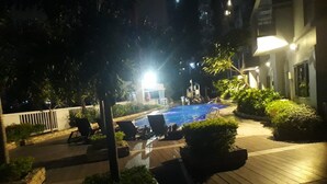A nighttime view of a swimming pool area with lounge chairs and potted plants.