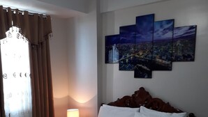 A hotel room with a bed, a nightstand with a lamp, and a cityscape artwork on the wall.