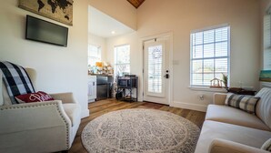 A spacious living room with a round rug, a sofa, and a chair. A kitchen is visible in the background with a refrigerator and microwave.